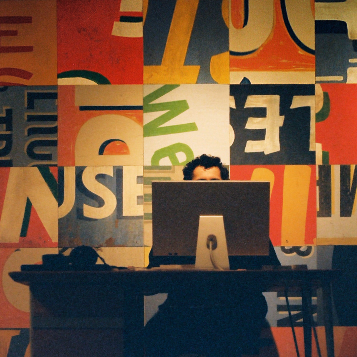 Aaron at a desk in front of a wall of painted letters